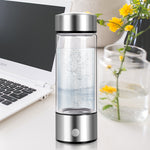 Silver and clear glass water bottle on a desk with a laptop and flowers in the background