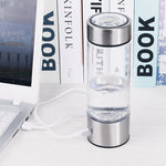 Clear water bottle with silver base and top on a white surface with books in the background
